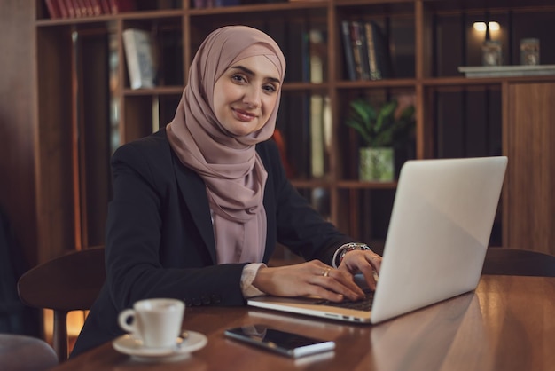Una feliz mujer de negocios musulmana usando una computadora portátil mientras trabaja en la oficina