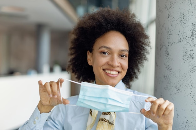 Feliz mujer de negocios negra con mascarilla protectora y mirando a la cámara