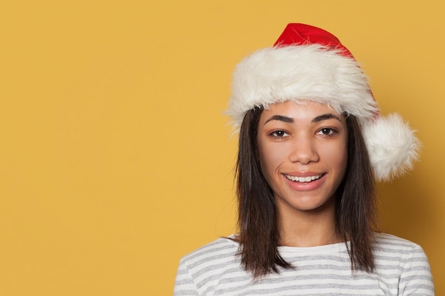 Feliz mujer negra sonriente con sombrero de Papá Noel en fondo amarillo