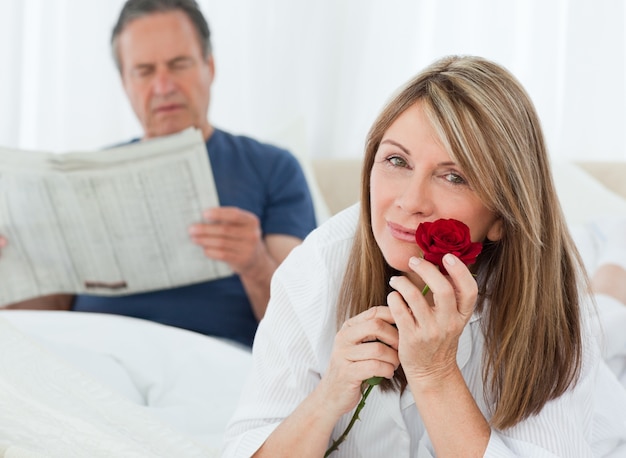 Foto feliz mujer oliendo su rosa mientras su marido está leyendo un periódico