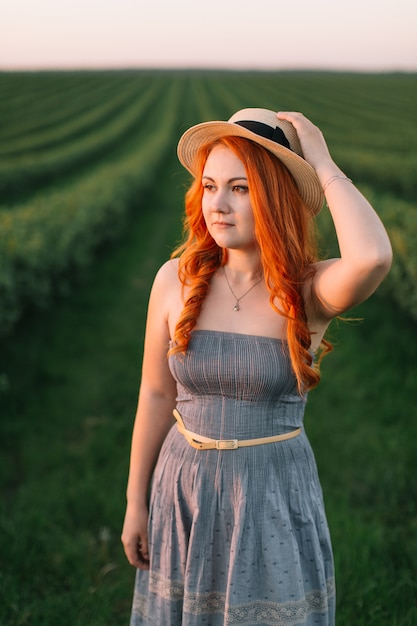 Feliz mujer pelirroja con un sombrero en un campo verde