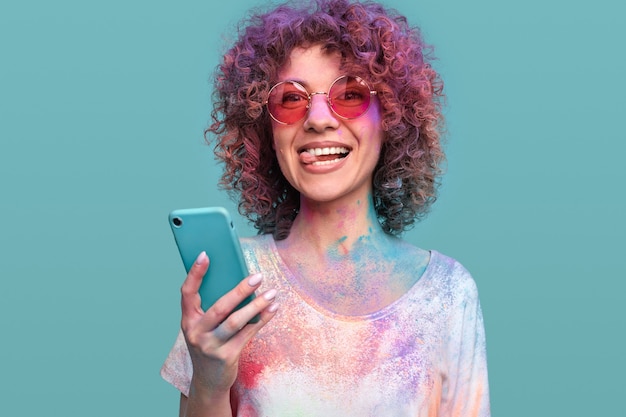 Feliz mujer de pelo rizado con colores Holi con smartphone