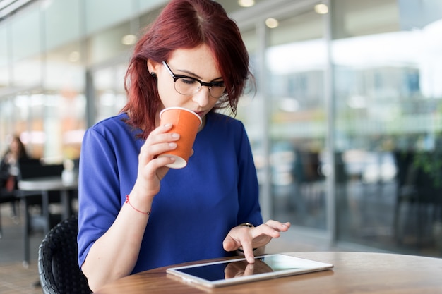 Feliz mujer pensativa pensando en la terraza de una cafetería en la calle mientras usa una tableta