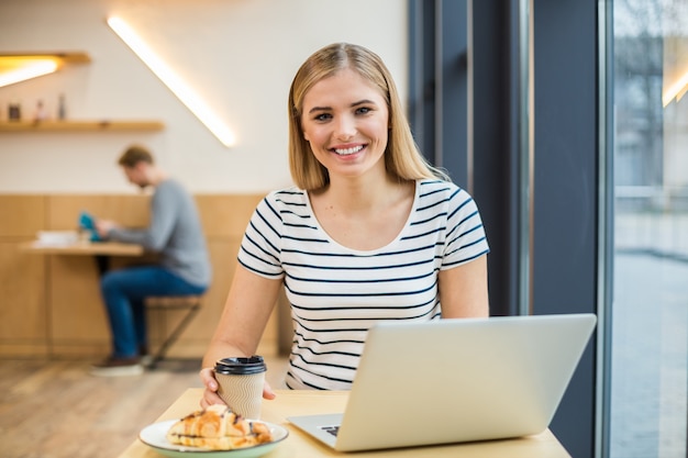 Feliz mujer positiva encantada sentada en la mesa y tomando un café mientras disfruta de su bebida