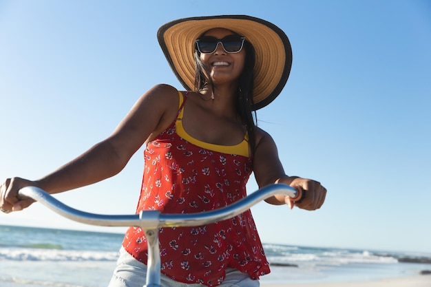 Feliz mujer de raza mixta divirtiéndose en vacaciones en la playa en bicicleta. tiempo de vacaciones de ocio al aire libre junto al mar.