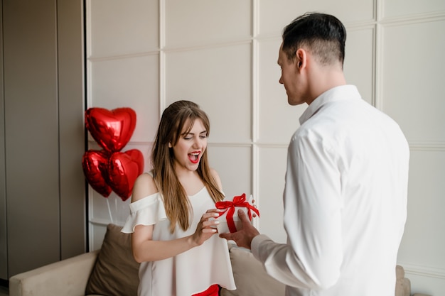 Feliz mujer recibe un regalo del hombre con globos rojos en forma de corazón en casa