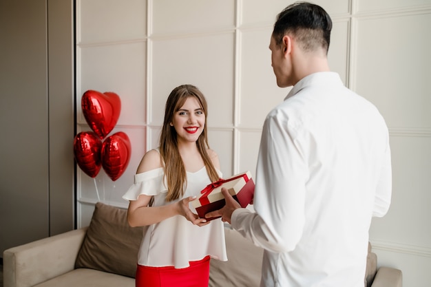 Feliz mujer recibe un regalo del hombre con globos rojos en forma de corazón en casa