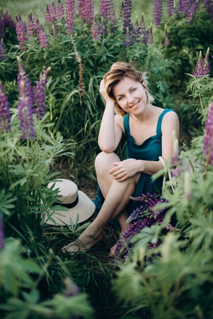 Feliz mujer romántica en un campo de flores de altramuces púrpuras coquetea y sonríe.