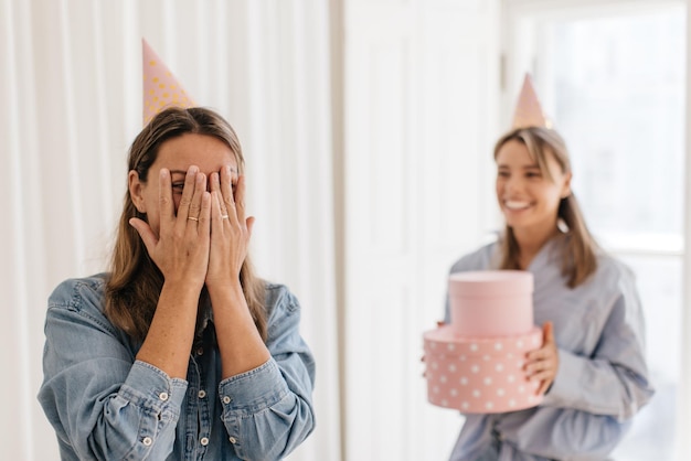 Feliz mujer rubia caucásica adulta que recibe un regalo de su amiga mientras cierra los ojos en el interior. Concepto de cumpleaños y amistad femenina