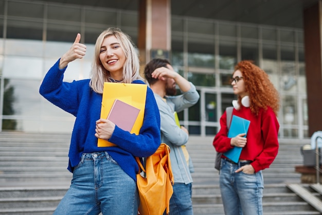 Feliz mujer rubia con cuadernos cerca de compañeros de clase