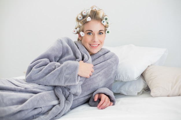 Foto feliz mujer rubia relajada en bigudíes de pelo acostado en su cama