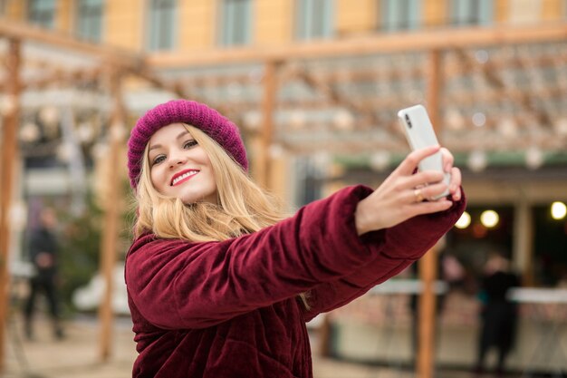 Feliz mujer rubia vestida con ropa de abrigo haciendo selfie en el fondo de garland en Kiev