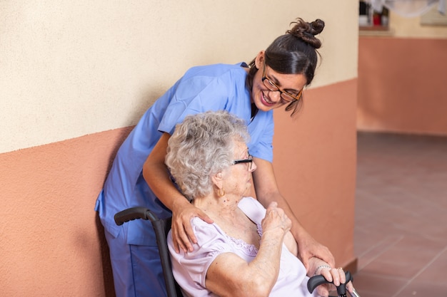 Feliz mujer senior con bastón en silla de ruedas con su cuidador en casa