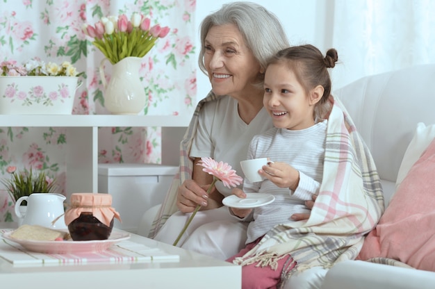 Feliz mujer senior con nieta con té en casa