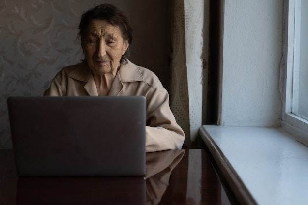 Feliz mujer senior sentada con su nieta mirando portátil haciendo videollamadas. Señora madura hablando por webcam, haciendo chat en línea en casa durante el autoaislamiento. Tiempo en familia durante Corona