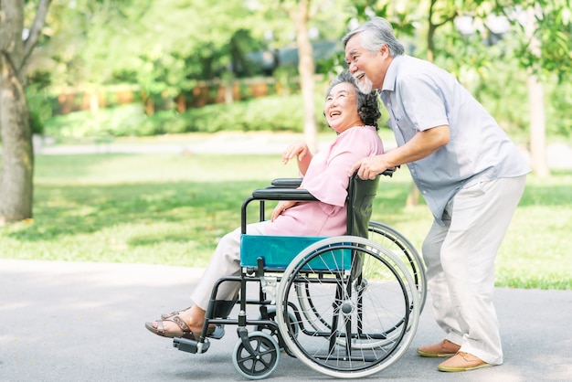 Feliz mujer senior en una silla de ruedas caminando con su esposo