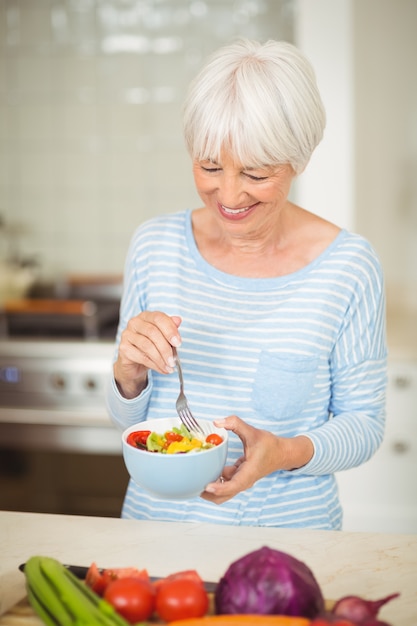 Feliz mujer senior sosteniendo tazón de ensalada de verduras