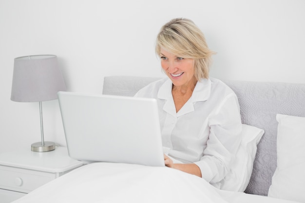 Feliz mujer sentada en la cama con la computadora portátil