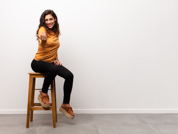 Feliz mujer sentada en una silla junto a la pared en blanco con copyspace