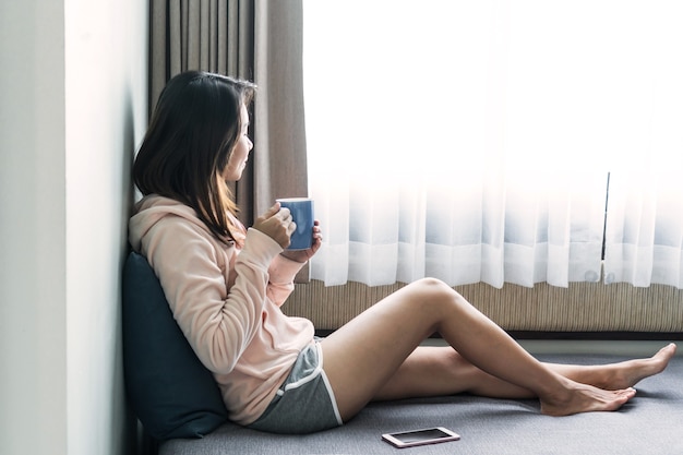 Feliz mujer sentada en el sofá y bebiendo café caliente por la mañana