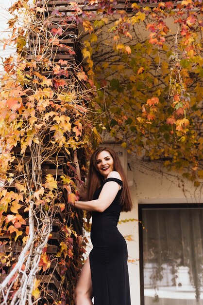 Feliz mujer sexy en un costoso vestido negro posando fuera de la casa, caminando en el jardín