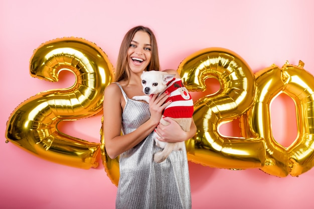 Feliz mujer sonriente con chihuahua perro blanco y globos de Navidad 2020 aislados en rosa