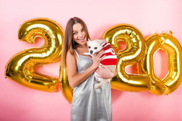 Feliz mujer sonriente con chihuahua perro blanco y globos de Navidad 2020 aislados en rosa