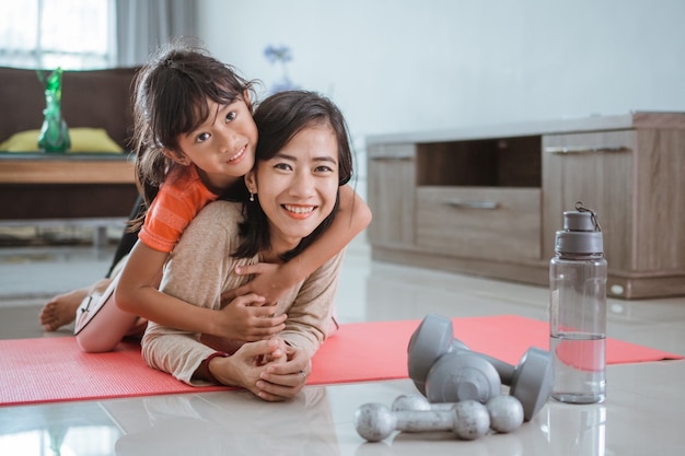 Feliz mujer sonriente e hija mirando a la cámara mientras hacen ejercicio juntos en casa