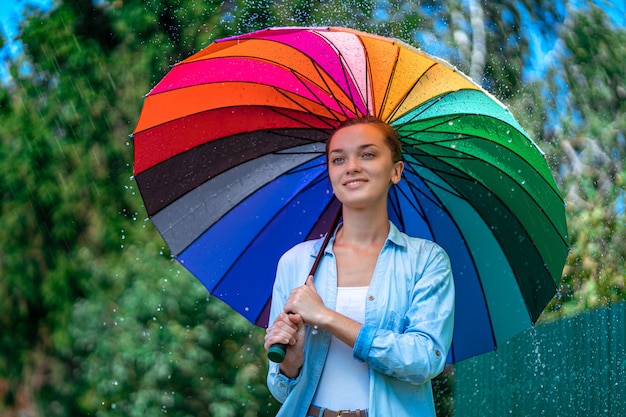 Feliz mujer sonriente con paraguas de colores durante la lluvia de verano