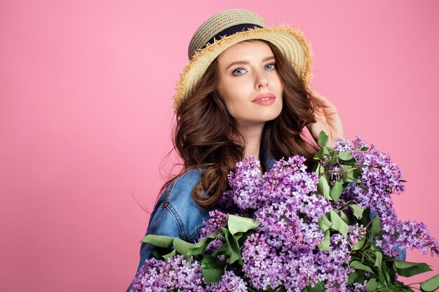 Feliz mujer sonriente en sombrero de paja posando con ramo de flores lilas