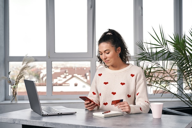 Feliz mujer sonriente con teléfono rojo y tarjeta de crédito comprando en internet compras en línea