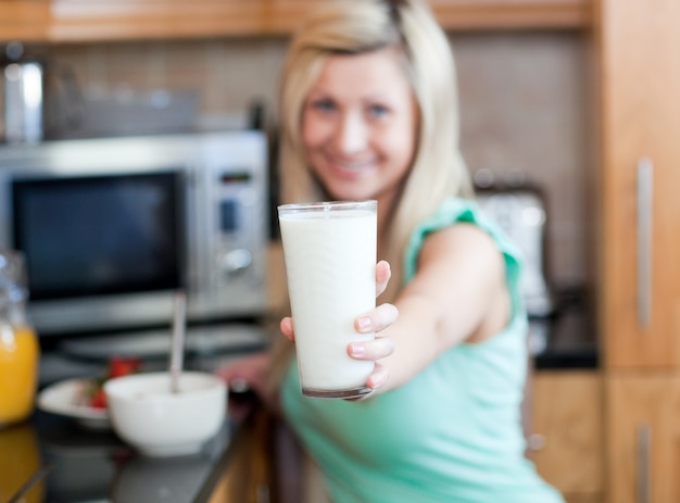 Feliz mujer sosteniendo un vaso de leche mientras toma un desayuno saludable