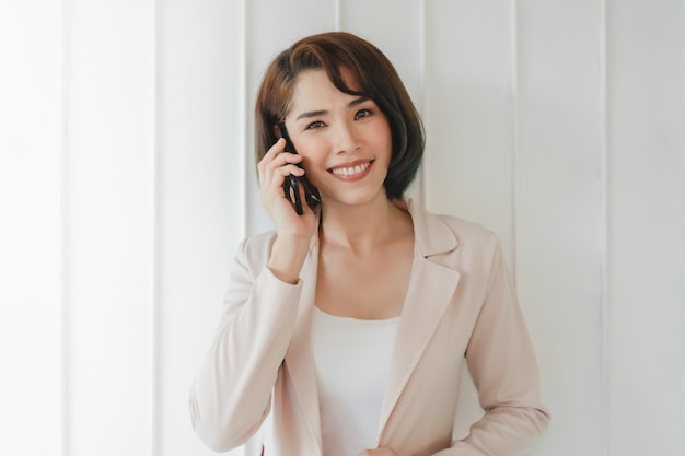 Feliz mujer trabajadora asiática está teniendo una conversación de teléfono inteligente