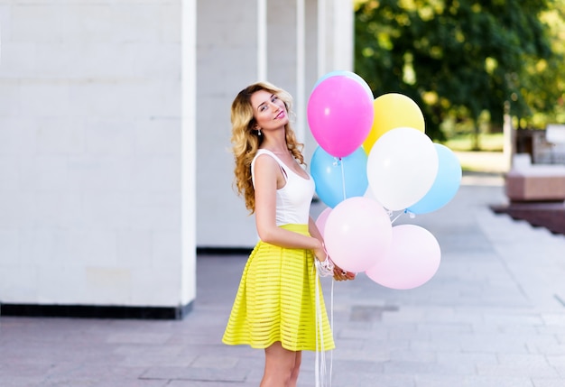 Feliz mujer en vestido amarillo con globos de colores
