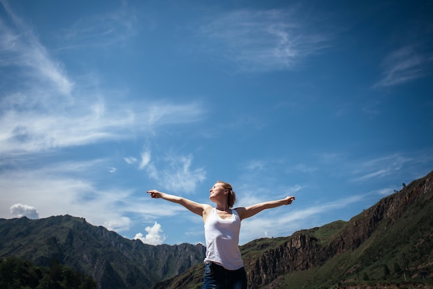 Feliz mujer viajera en una camiseta blanca contra las hermosas montañas y el cielo azul