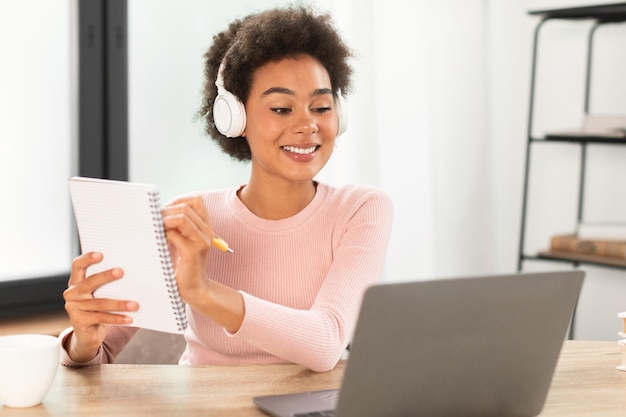 Feliz mulher afro-americana milenar em fones de ouvido sem fio mostra notebook para laptop de webcam