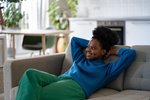 Feliz mulher afro-americana relaxada, deitada no sofá com as mãos atrás da cabeça e olhando para frente