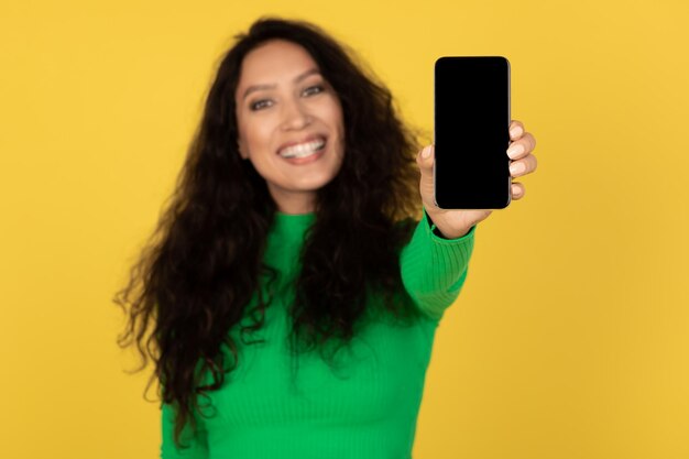 Feliz mulher árabe mostrando o telefone com fundo amarelo de tela vazia