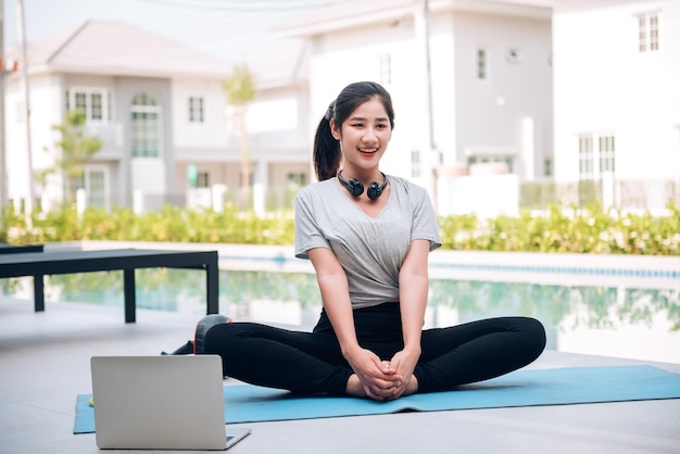 Feliz mulher asiática esticando exercícios e exercícios de ioga pela manhã em casa ao ar livre