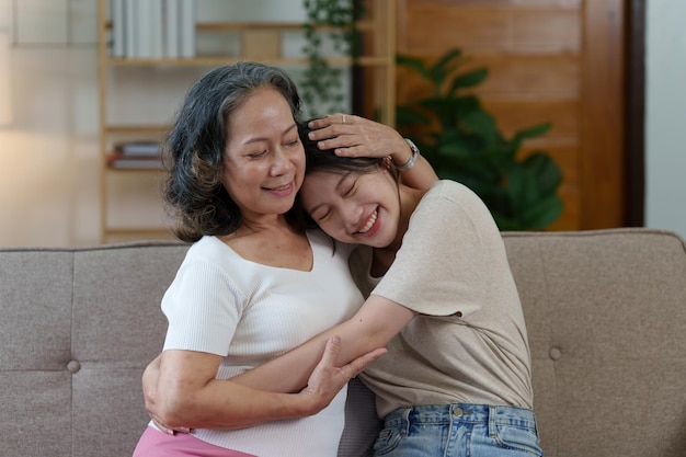 Feliz mulher asiática sênior e sua filha adulta estão abraçando no sofá
