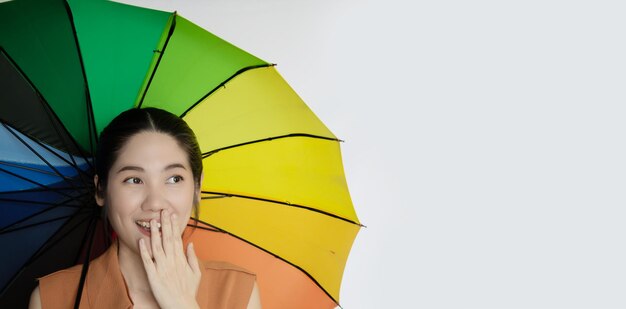 Feliz mulher asiática sorridente sob um guarda-chuva colorido e cobrir a boca com a mão com um sorriso positivo