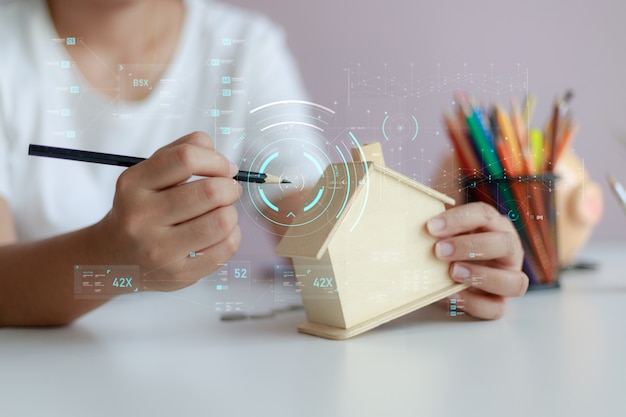 Feliz mulher asiática usando lápis para desenhar com cofrinho de casa de madeira e tecnologia cyber