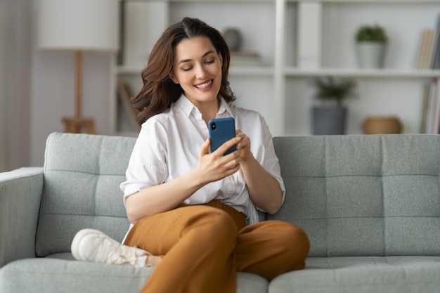 Feliz mulher bonita casual está usando um telefone sentado em um sofá em casa