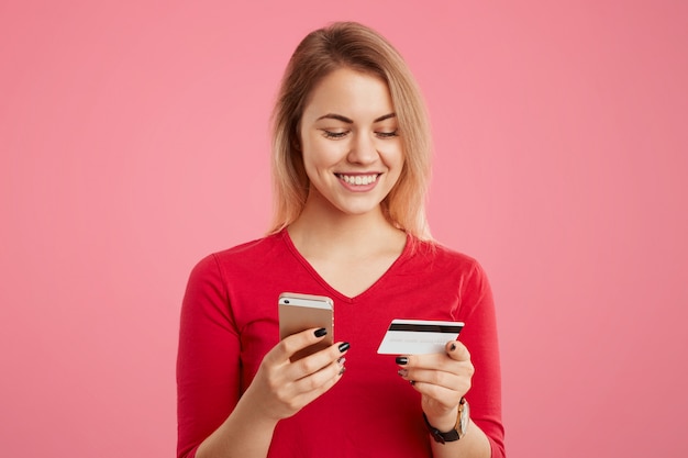 Feliz mulher bonita possui telefone inteligente e cartão de crédito