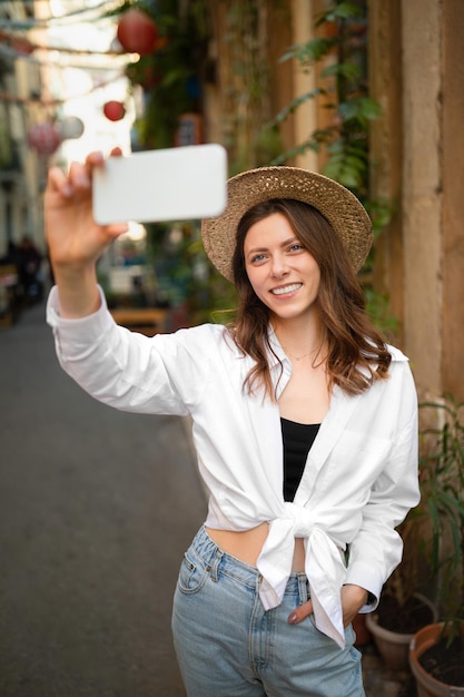 Feliz mulher caucasiana do milênio em casual e chapéu faz foto em smartphone olha para pontos turísticos na nova cidade lá fora