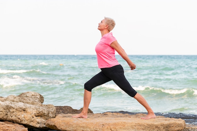 Feliz mulher de meia idade à beira-mar fazer exercícios de alongamento. retrato de vista lateral