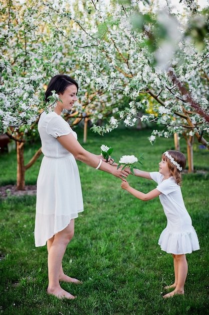 Feliz mulher e criança, linda filha e mãe no jardim de flor de primavera, usando um vestido branco ao ar livre, a temporada de primavera está chegando. Conceito de feriado do dia das mães