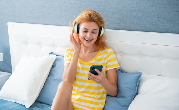 Feliz mulher em fones de ouvido ouve música no telefone mulher em casa ouve música em fones de ouvido mulher usando fones de ouvido para ouvir música