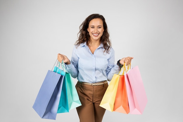 Foto feliz mulher europeia adulta com roupa formal, segurando muitas sacolas de compras, desfrutando de compras