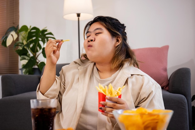 Feliz mulher gorda asiática gosta de comer deliciosas batatas fritas e batatas fritas na sala de estar